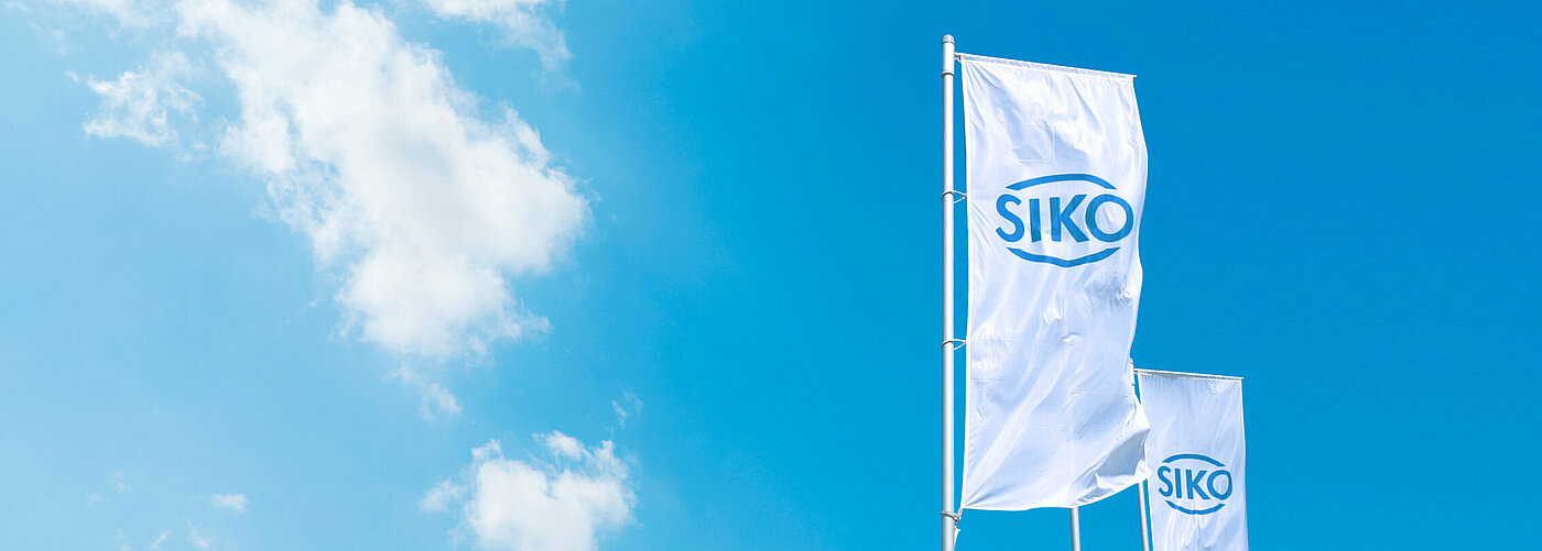 White Siko flag with blue logo against a blue sky with sunshine